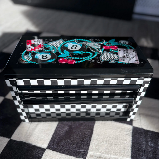 Black metal makeup and jewelry toolbox with black and white checkered sides and graphic lid featuring 8-ball, playing cards, and cherry designs, from Moonlight Market